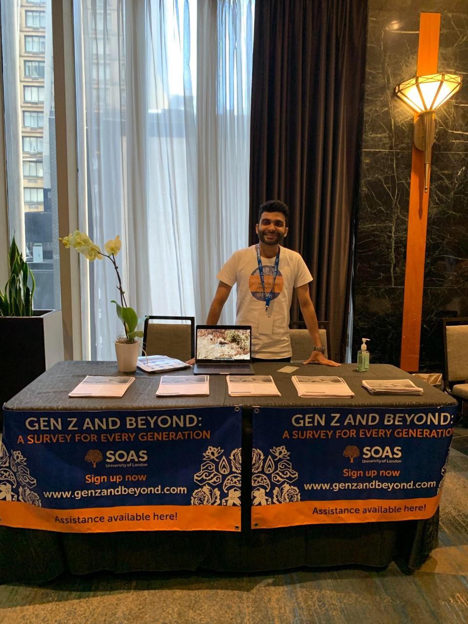 Sheherazad Pavri stands behind a table with a laptop and documents at the World Zoroastrian Congress.