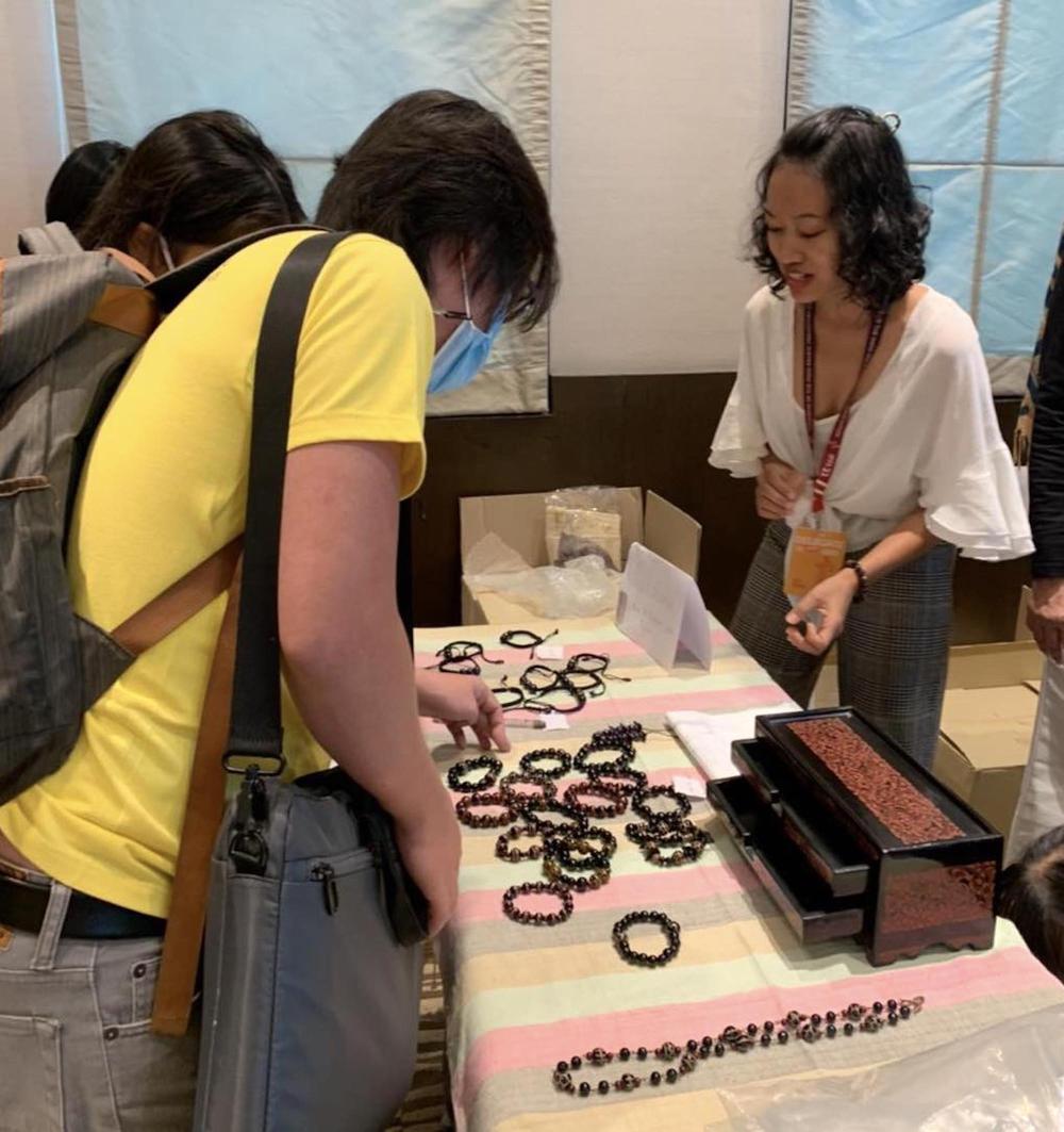Figure 7. Theint Theint Aung with 'Laksharas' stall and Udomluck Hoontrakul wearing new bracelet (Photo Pwint Phu Maung, Alumni)