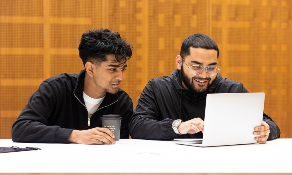 Two students talking and looking at a laptop