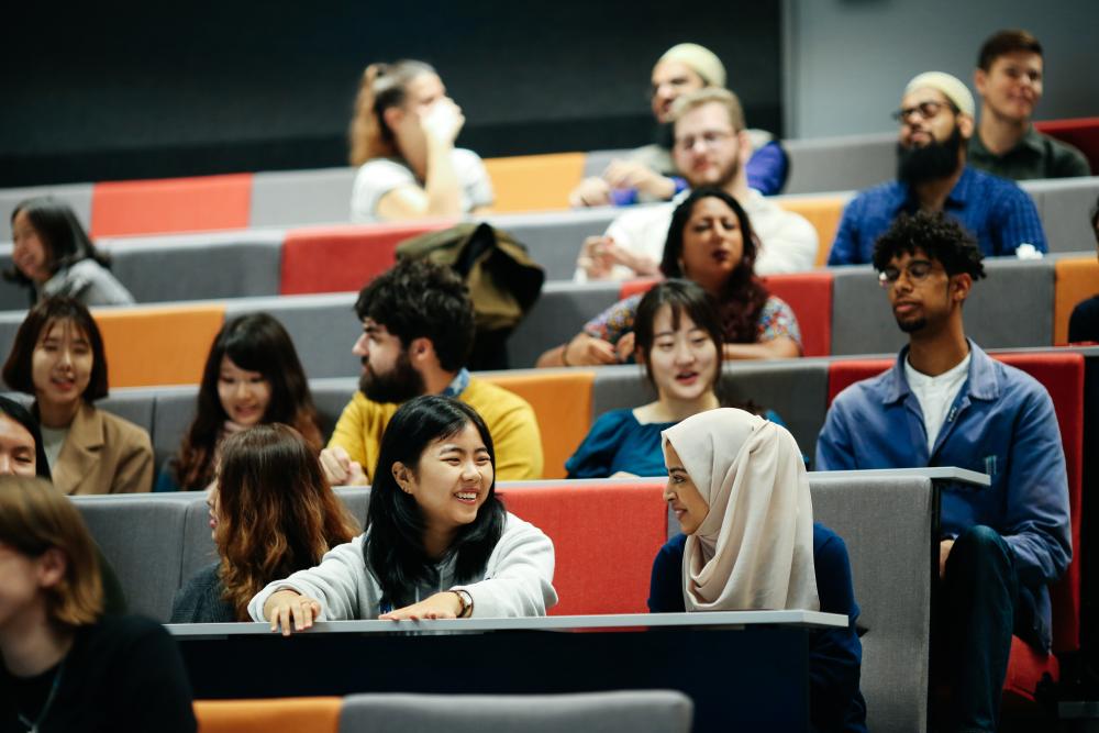 Two students talk to each other and smile in lecture theatre