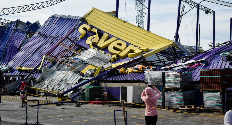 A woman stands in front of a building that has been blown over