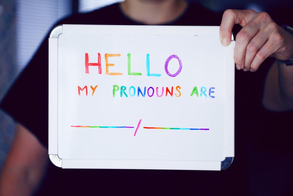 A person holds up a sign that says "hello, my pronouns are..."