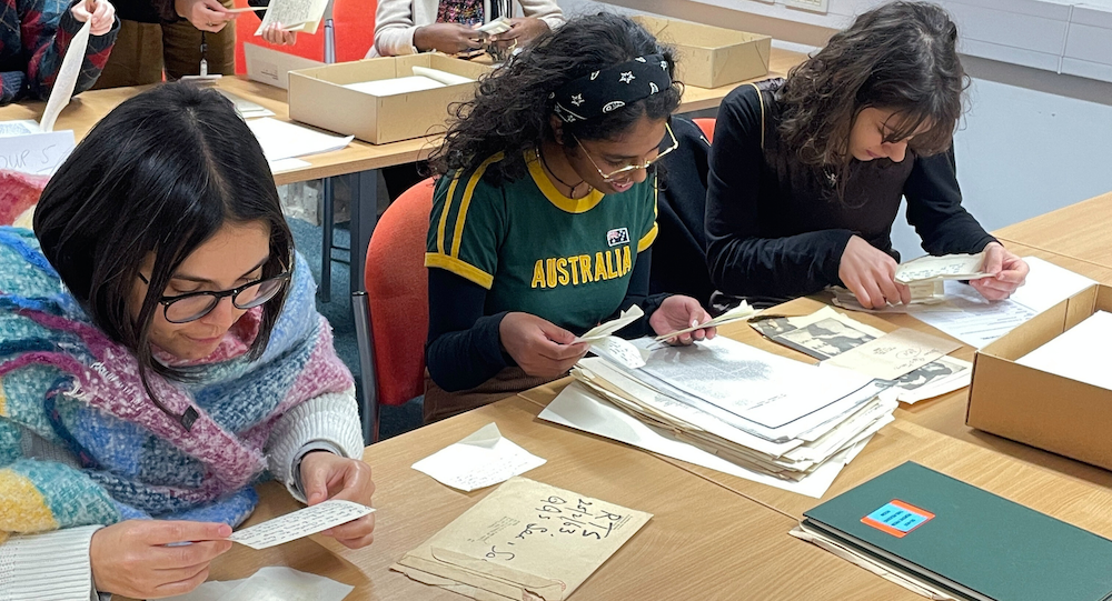 Three students at a desk looking through archive materials in class