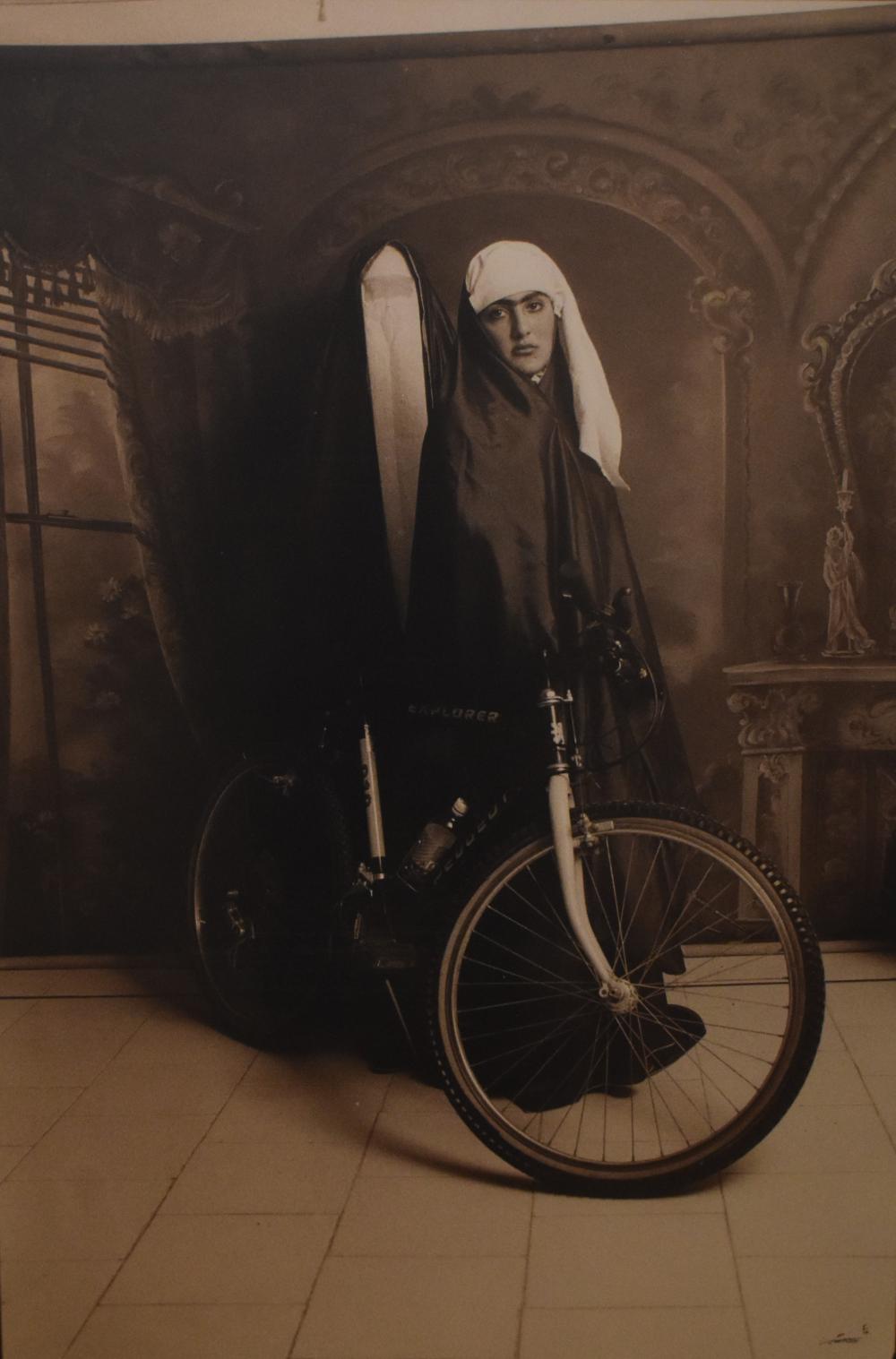 a black and white art photograph of a woman in Qajar style clothing, with a bicycle