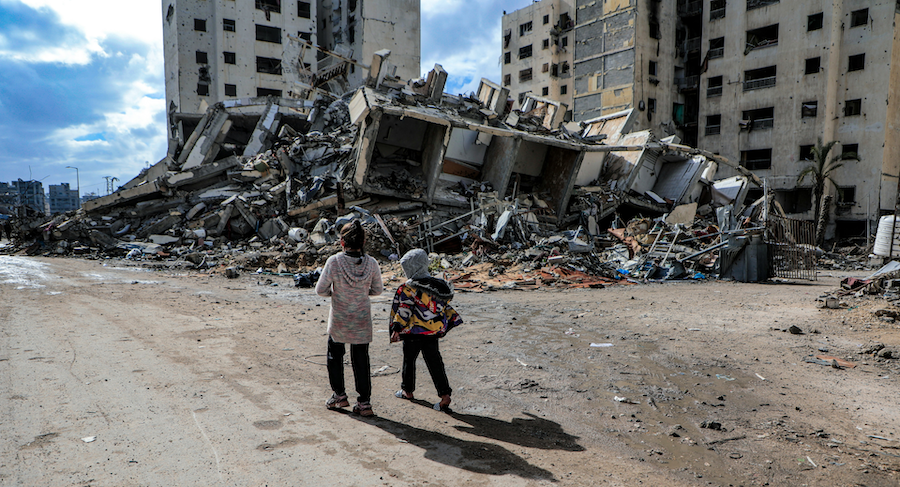 Two children walk in the streets of Gaza with rubble surrounding them