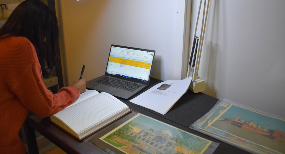 A student writing on paper with archive material around her