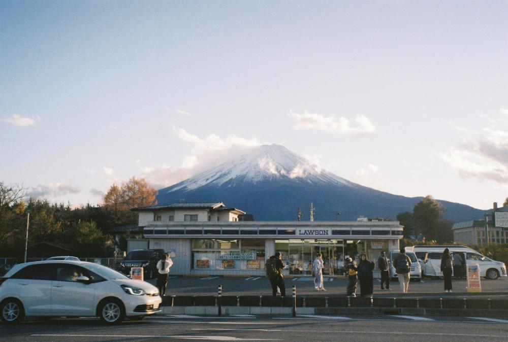 3.	Mount Fuji creates a serene backdrop to a Lawson convenience store with people milling about.