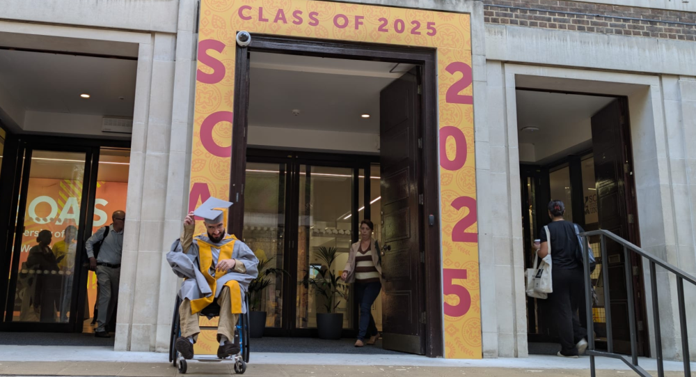 Ali in a graduation outfit outside the front entrance of SOAS