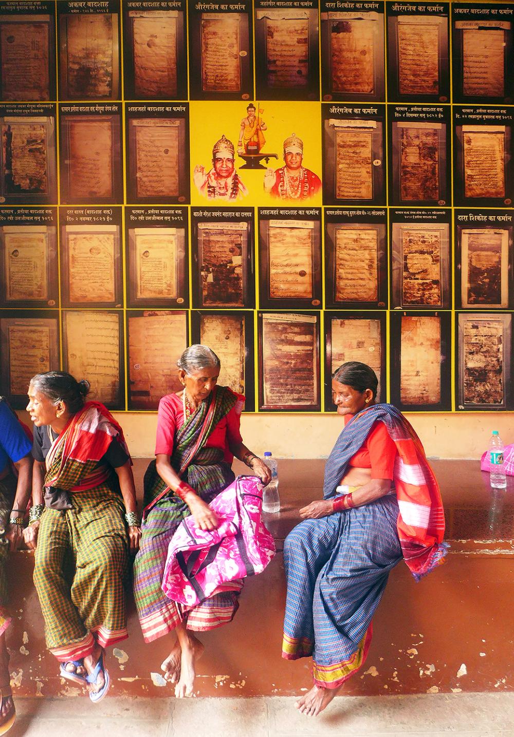 Photograph of three women sitting in front of images of historical Mughal documents