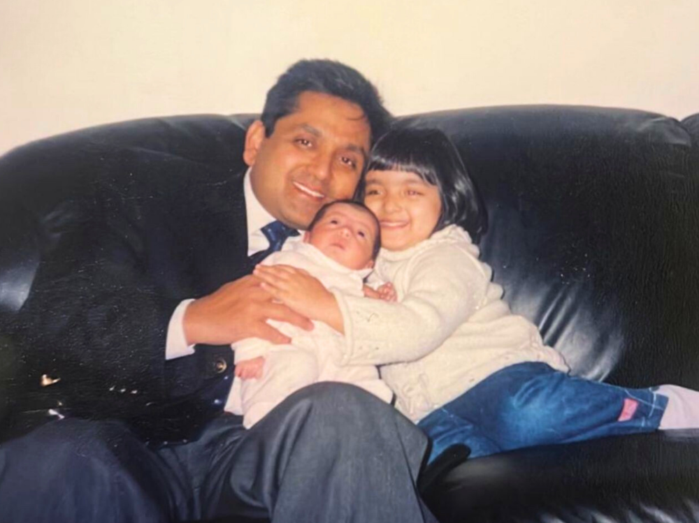 A person sitting on a black leather sofa holding two small children close, with the children leaning in on either side.