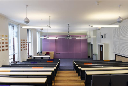 Two rows of black seats and white tables with purple wall on far side.