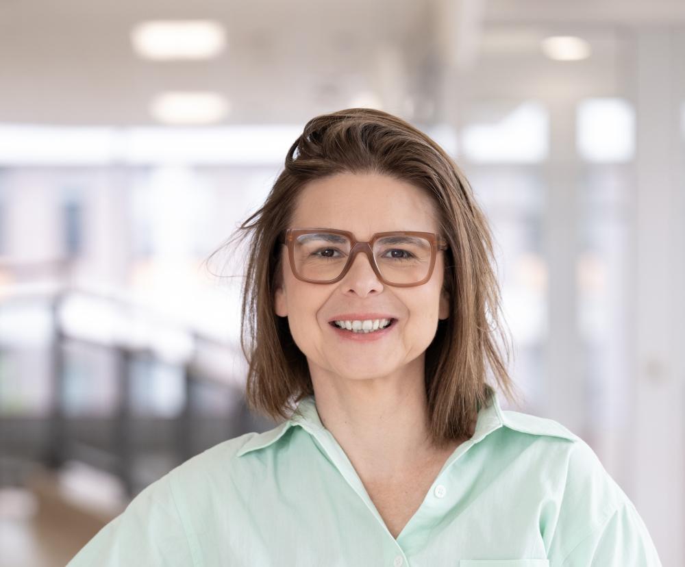 A woman standing wearing glasses, standing indoors