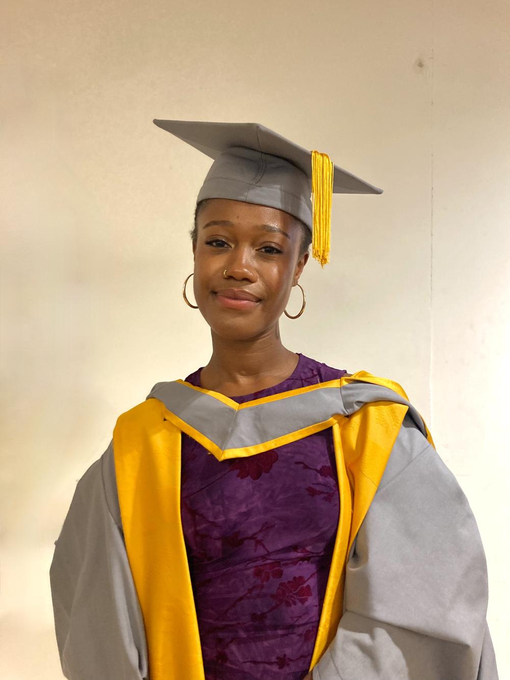 A graduate wearing a grey and yellow gown 